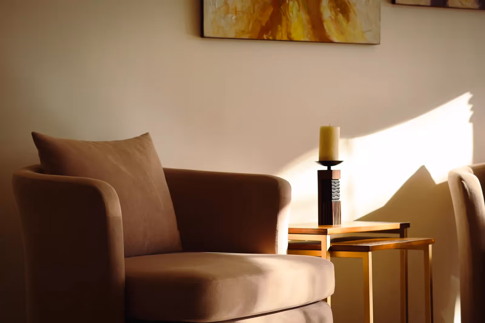 A soft armchair in warm sunlight against a calm, neutral wall